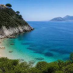 Vue d'une crique aux eaux turquoise cristallines, avec une colline verdoyante et des maisons blanches perchées, près d'une île à côté de Capri.