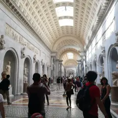 Visiteurs admirant des sculptures dans un long couloir orné de bustes et de bas-reliefs. Une excellente façon de savoir comment aller au Vatican.