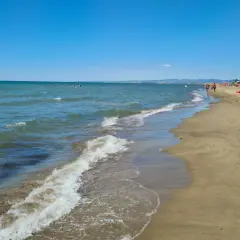 Plage de Fregene, mer bleue, sable doré, parasols et baigneurs profitant du soleil.