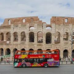 Un bus touristique rouge vif circule devant le Colisée à Rome, transportant des visiteurs pour une visite de la ville.