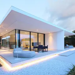 Villa moderne à Jesolo avec grandes baies vitrées, terrasse illuminée et mobilier extérieur invitant.
