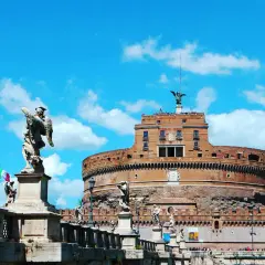 Le **château** Sant'Angelo à **Rome**, avec ses statues d'anges sur le pont, se dresse sous un ciel bleu éclatant.