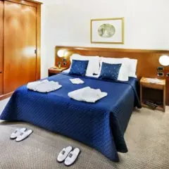 Chambre confortable à l'hôtel Ponte Sisto Rome avec lit bleu, peignoirs et pantoufles.