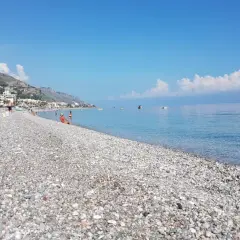 Plage de galets à Letojanni, Sicile. Des baigneurs profitent du soleil sous un parasol, tandis que la mer d'un bleu profond s'étend à l'horizon.