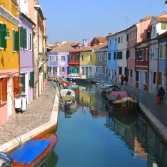 Canal bordé de maisons colorées à Murano, Venise. Des bateaux sont amarrés le long de la voie navigable, reflétant les façades vibrantes.