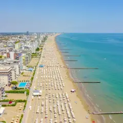 Vue aérienne de la longue plage de Lido di Jesolo, avec des rangées de parasols blancs, des hôtels et la mer Adriatique bleue.