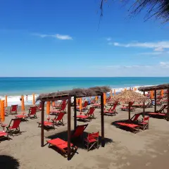 Plage de Marina di Bibbona avec des chaises longues rouges et des parasols de paille sous un ciel bleu éclatant.