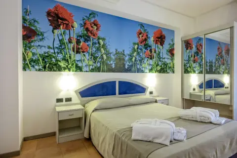 Chambre d'hôtel Antares Sicile avec fresque de coquelicots rouges. Peignoirs blancs et chaussons prêts pour les clients.