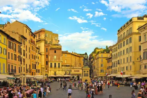Place animée de Campo de' Fiori à Rome, avec des terrasses de café, des bâtiments colorés et une statue au centre.