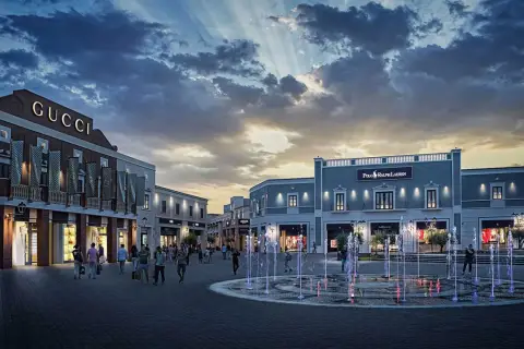 Un soir à l'outlet Sicile, les fontaines illuminées dansent sous un ciel dramatique, devant les boutiques Gucci et Polo Ralph Lauren.