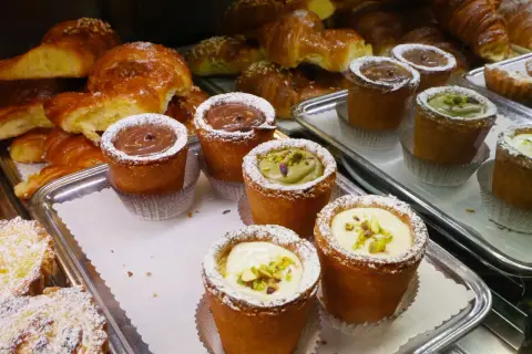 Pâtisseries variées, dont des croissants dorés et des petits gâteaux garnis de crème au chocolat, de pistache ou de crème pâtissière, dans un restaurant florentin.