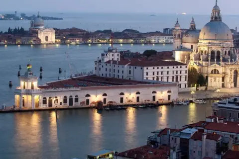Vue de Venise au crépuscule, avec la basilique Santa Maria della Salute et le bâtiment de la Fondation Pinault Venise illuminés.