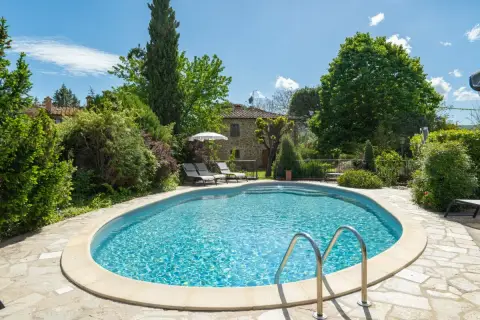 Magnifique piscine dans un jardin luxuriant, typique d'une location en Toscane. Le soleil brille sur l'eau bleue, invitant à la détente.
