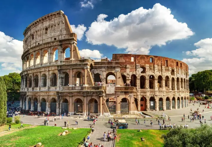 Le Colisée de Rome en août, baigné de soleil, accueille des visiteurs sous un ciel bleu parsemé de nuages.