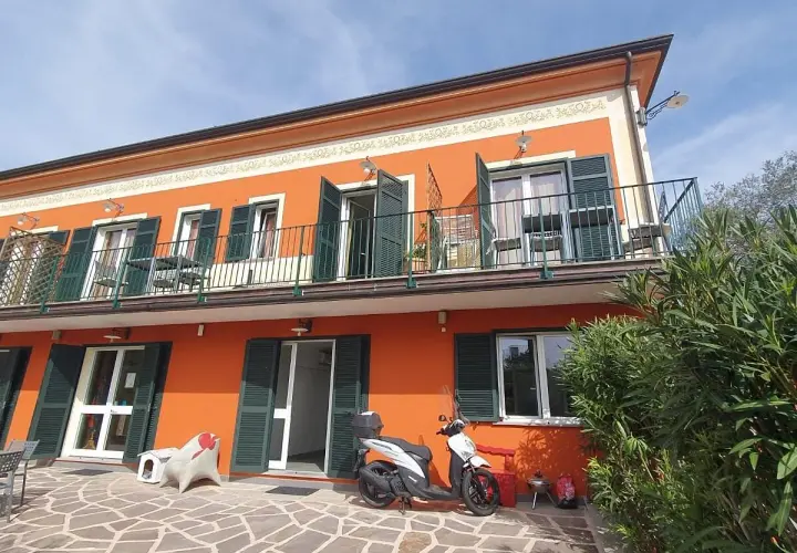 Façade orange vif de l'hôtel Olivium La Spezia avec balcons, volets verts et scooter blanc sur la terrasse pavée.