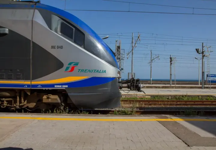 Le train Trenitalia ME 040, prêt à partir pour un voyage en train en Sicile, attend sur les rails sous un ciel bleu clair.