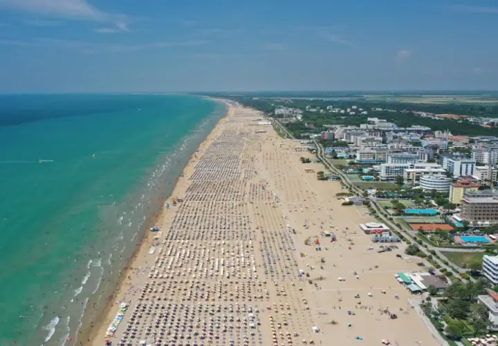 Plage bondée de parasols et de baigneurs à Bibione, Italie, avec la mer turquoise et des hôtels en arrière-plan.