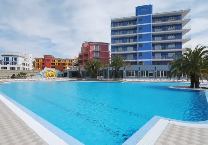 Vaste piscine bleue devant des bâtiments colorés et un grand gonflable de Bob l'éponge, au village ai pozzi.