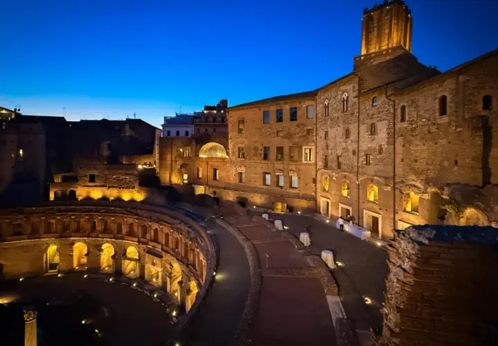 Les marchés de Trajan s'illuminent dans la nuit romaine, vestiges antiques baignés d'une douce lumière dorée sous un ciel bleu profond.