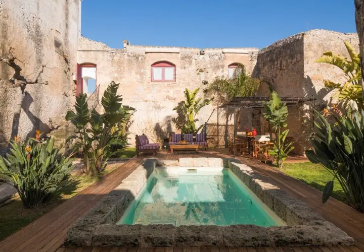 Cour intérieure d'une masseria en Italie, avec piscine, mobilier de jardin et végétation luxuriante.