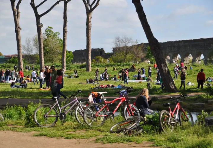 Des vélos garés près d'un parc à Rome, où des gens profitent du soleil et des ruines antiques.