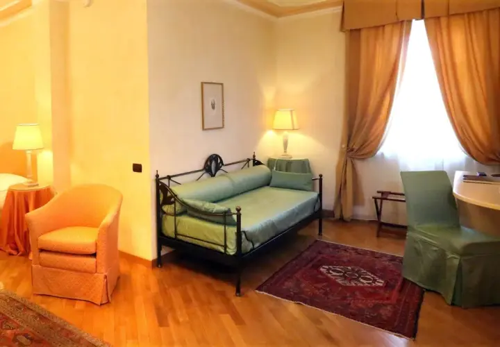 Chambre confortable dans un des hôtels de Castiglione Tinella, avec un lit de repos vert, un fauteuil orange et des rideaux dorés.