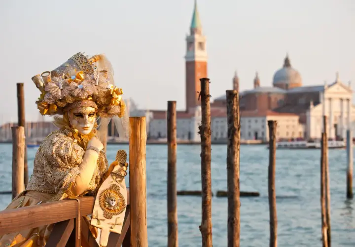 Une personne masquée et costumée, prête pour le carnaval, pose près de l'eau. Une belle image pour savoir quand aller à Venise.