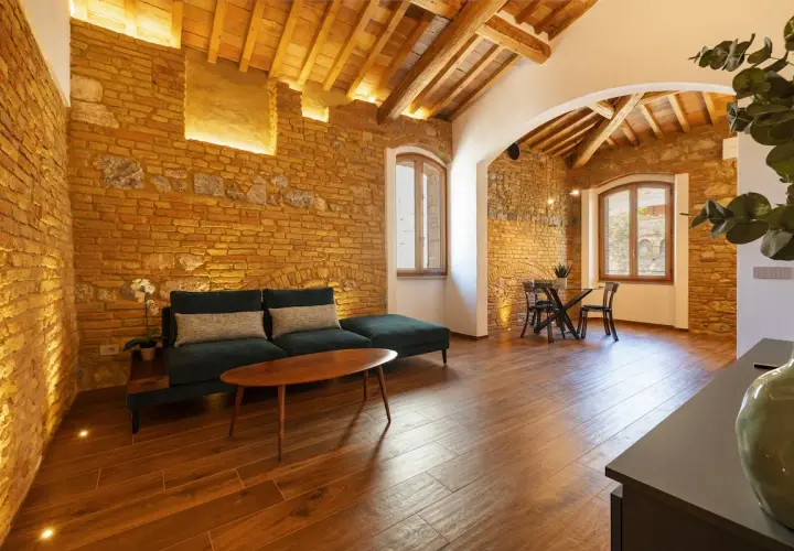 Salon de la villa Mazzanta avec murs en briques apparentes, poutres au plafond, canapé confortable et table à manger.