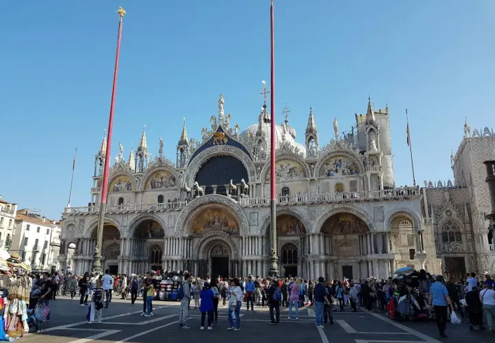 La place animée devant la magnifique église de Venise, avec ses dômes et ses mosaïques, sous un ciel bleu éclatant.