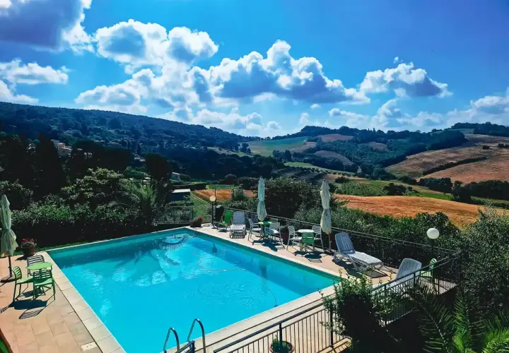 Piscine étincelante devant une **ferme toscane** pittoresque, avec des collines ondulantes et un ciel bleu éclatant.