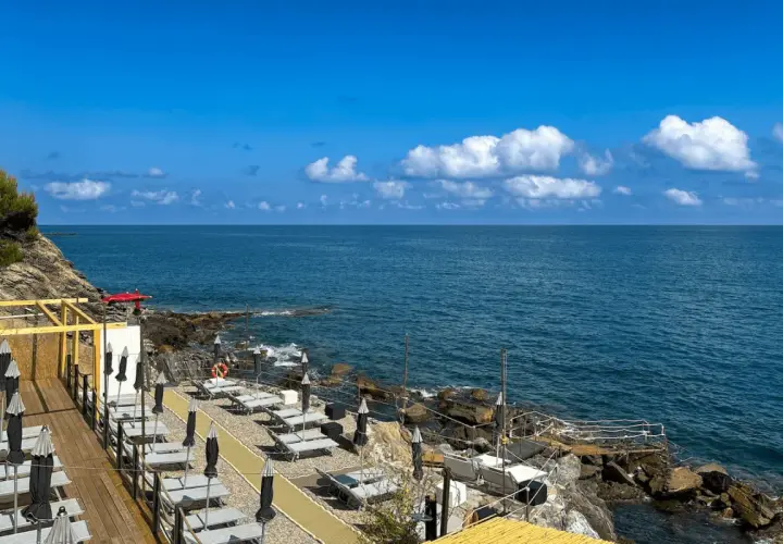 Plage aménagée à San Bartolomeo al Mare, avec chaises longues et parasols face à la mer bleue sous un ciel d'été.