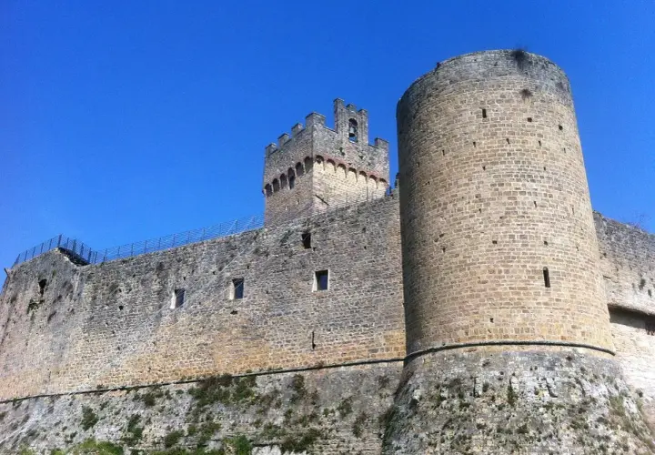 Château médiéval imposant à Poggibonsi, Italie, avec ses tours rondes et carrées sous un ciel bleu éclatant.