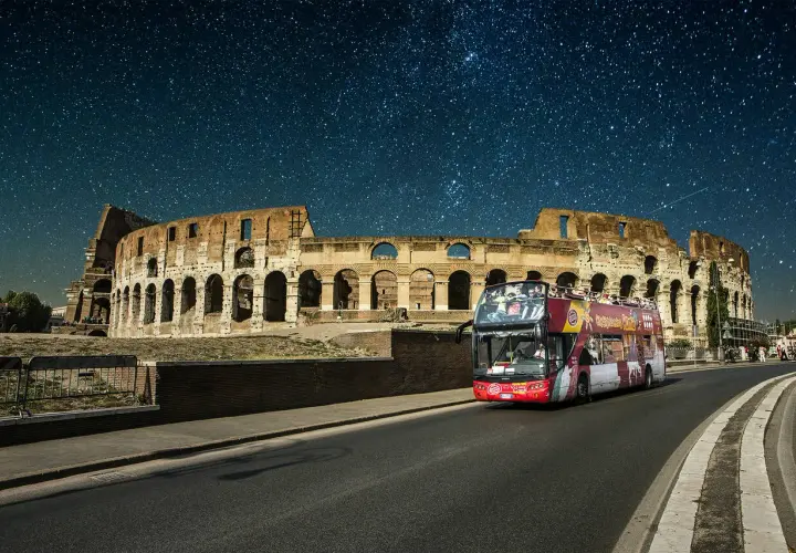 Un bus de nuit Rome passe devant le Colisée sous un ciel étoilé.