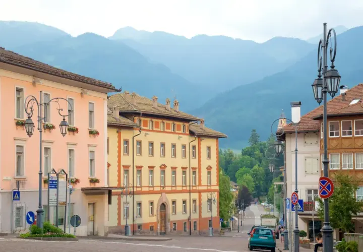 Vue d'une rue à Cavalese, Italie, avec des bâtiments colorés et des montagnes en arrière-plan.