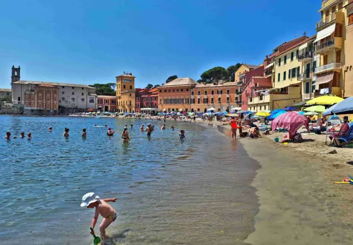 Plage animée à Chiavari, Italie, avec des baigneurs dans l'eau et des parasols colorés sur le sable.