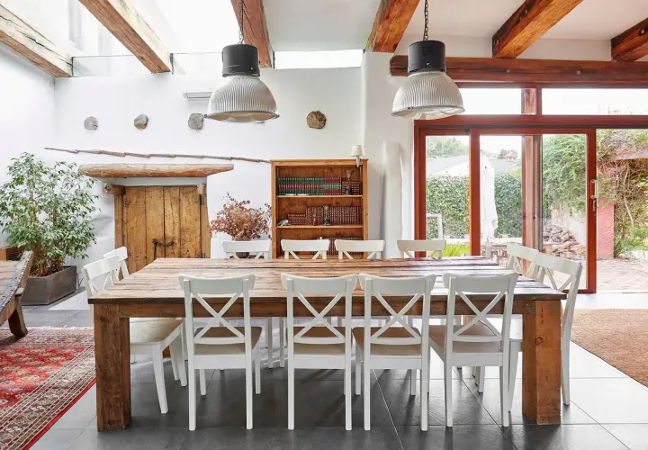 Salle à manger rustique d'un agriturismo en Ligurie, avec table en bois massif, chaises blanches et grande porte vitrée donnant sur le jardin.