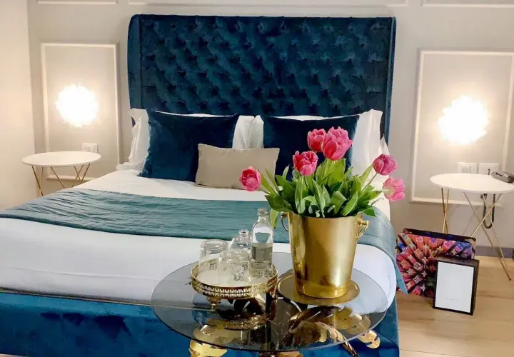 Chambre d'hôte en Lombardie : lit luxueux avec tête de lit capitonnée bleue, tulipes roses et tables de chevet élégantes.
