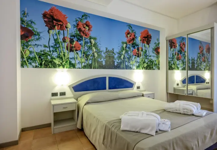 Chambre d'hôtel Antares Sicile avec fresque de coquelicots rouges. Peignoirs blancs et chaussons prêts pour les clients.