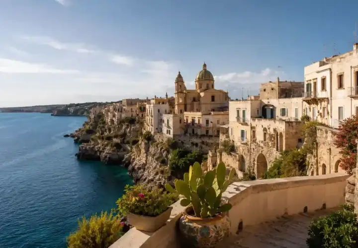 Vue d'une ville côtière italienne perchée sur une falaise, avec des maisons blanches et une église. Idéal pour une maison à louer en Italie.
