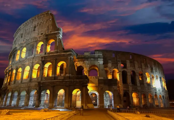 Le Colisée de nuit, illuminé par des lumières chaudes, se dresse sous un ciel aux couleurs flamboyantes.