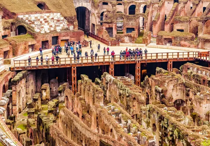 Vue d'ensemble de l'arène du Colisée à Rome, avec des touristes sur une passerelle surplombant les ruines antiques.