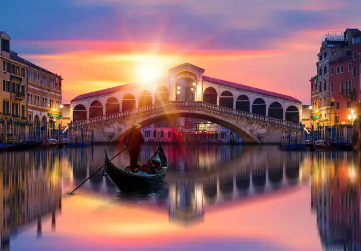 Gondole glissant sur le Grand Canal, sous un ciel aux couleurs vibrantes, avec le célèbre pont du Rialto en arrière-plan. Une scène qui évoque une célèbre peinture de Venise.