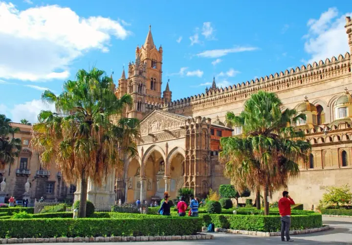 La cathédrale de Palerme, capitale Sicile, se dresse fièrement sous un ciel bleu, entourée de palmiers et de jardins verdoyants.