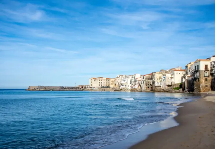 Vue de la plage et des maisons colorées de Cefalù, Sicile, sous un ciel bleu clair.