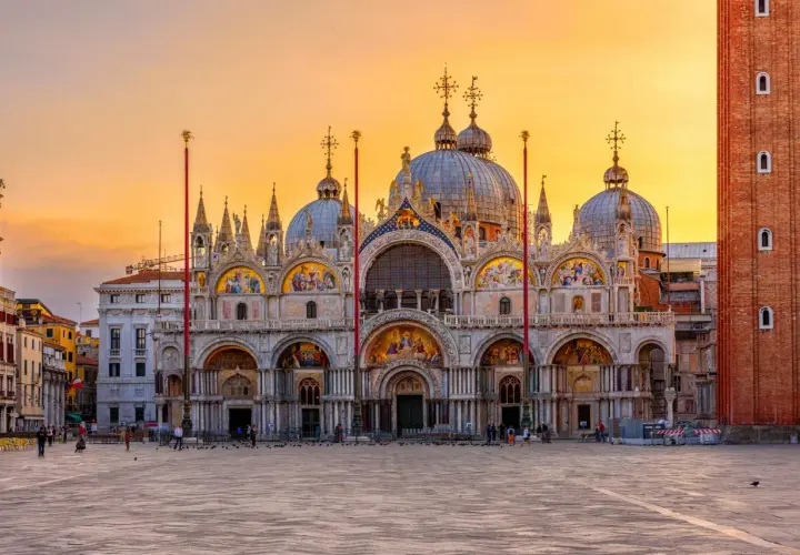 Magnifique coucher de soleil sur la place Saint-Marc, idéal pour visiter la basilique Saint-Marc. La façade ornée de mosaïques brille sous le ciel orangé.