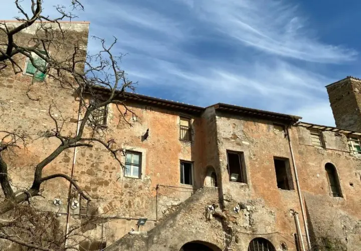 Bâtiments anciens et décrépits, avec une tour de briques penchée, sous un ciel bleu et nuageux. Une promenade sur la Via Appia à pied révèle ces ruines.