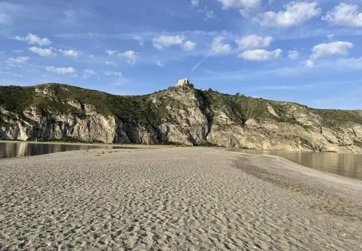Plage de Patti, Sicile. Un château domine la colline rocheuse surplombant la mer calme et la plage de sable.
