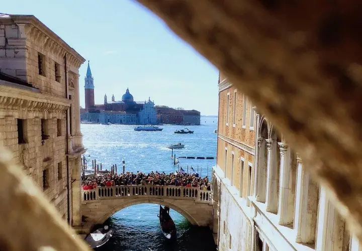 Vue d'un pont vénitien animé, avec des gondoles et des bateaux sur le canal, et des bâtiments historiques en arrière-plan.