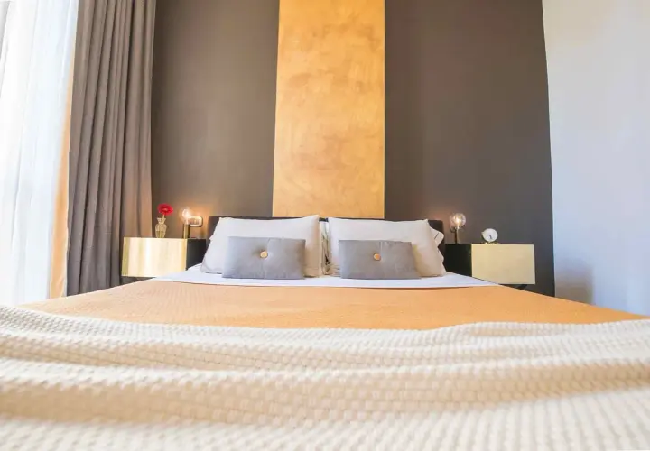 Lit et tables de chevet dorés dans une chambre d'hôte Italie du Nord. Rideaux gris et blancs, mur anthracite et ocre.