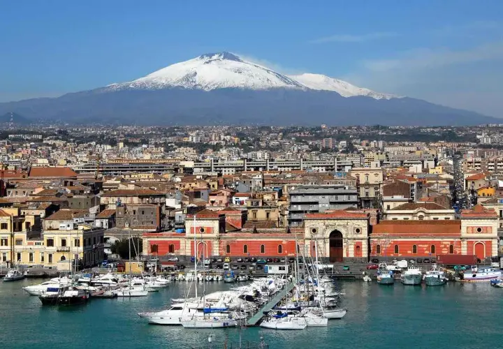 Vue panoramique de la ville de Catania, Sicile, avec le mont Etna enneigé en arrière-plan et un port rempli de voiliers.